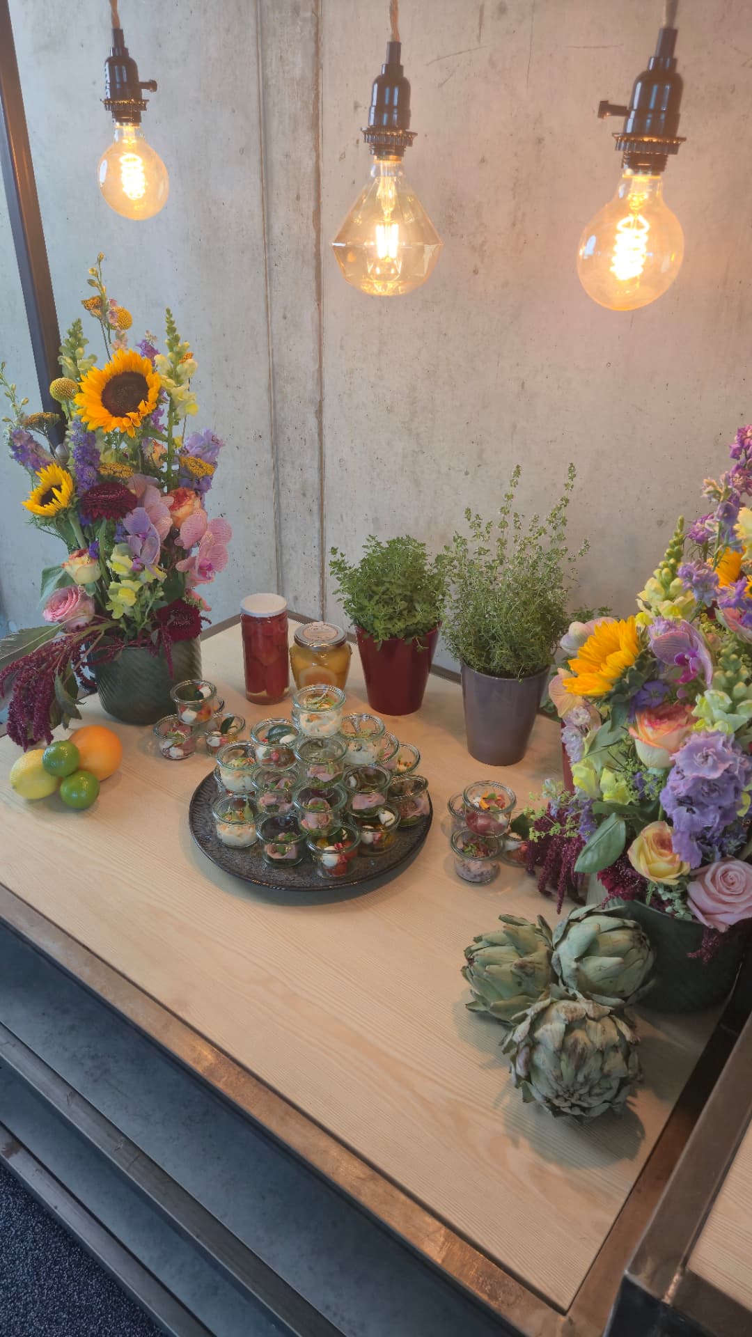 Fingerfood-Buffet mit bunten Gläschen, frischen Kräutern und Blumen auf einem Holztisch im Lofthouse-Stil